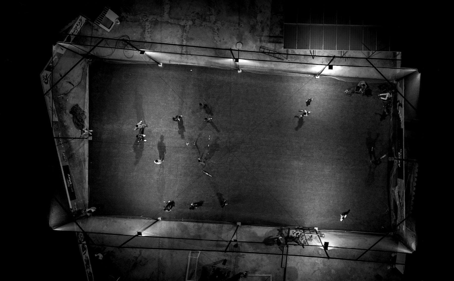 Vue aérienne d’un terrain de football urbain grillagé, éclairé de nuit